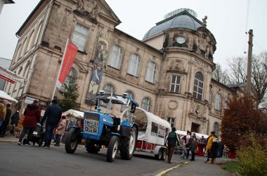 Ein altes Sandstein-Gebäude. Es ist das Spielzeugmuseum der Stadt Sonneberg. Davor steht ein Traktor mit Anhänger.