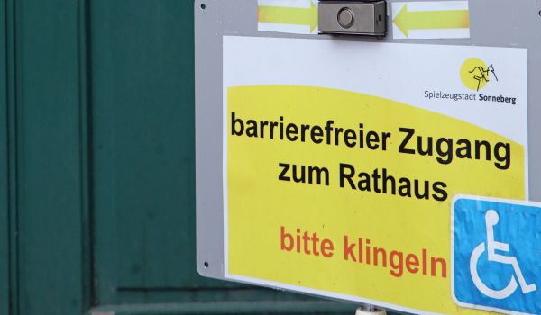 Ein gelbes Schild mit der Aufschrift barrierefreier Zugang zum Rathaus, bitte klingeln.