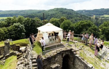 Ein Hochzeitspavillon steht auf einer Burgruine. Außenrum stehen Gäste.