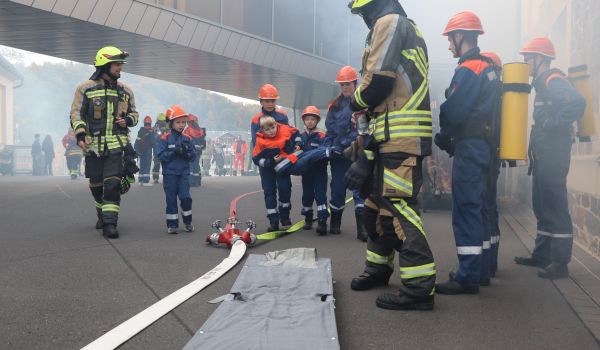 Ein Junge wird während einer Feuerwehrgroßübung von anderen Kindern und Jugendlichen gerettet.