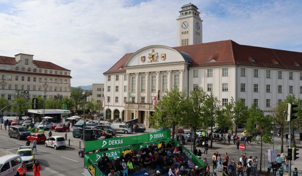 Vor dem Rathaus der Stadt Sonneberg stehen viele Autos. Im unteren Teil des Bildes steht eine Tribühne mit vielen Menschen darauf.