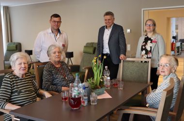 Drei Seniorinen sitzen an einem Tisch. Daneben stehen Mitarbeiter und der Bürgermeister der Stadt Sonneberg.