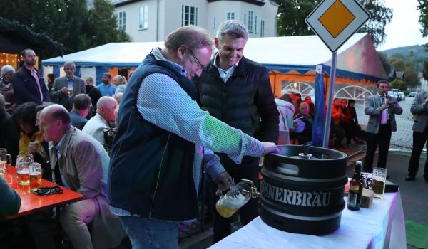 Zwei Männer stehen an einem Tisch. Der Mann links zapft Bier aus einem Fass. Der Mann danbenen ist der Bürgermeister der Stadt Sonneberg. Im Hintergrund sitzen viele Menschen auf Bierzeltgarnituren.