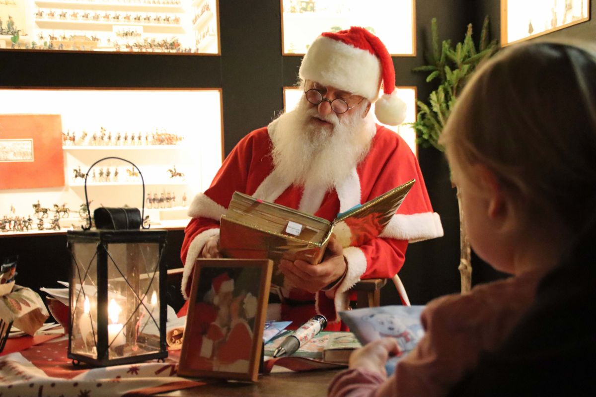 Ein Mann im Weihnachtsmannkostüm ließt einem Kind aus einem goldenen Buch vor.