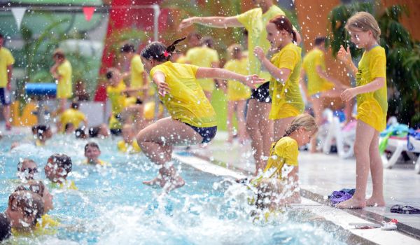 Kinder in gelben T-Shirts springen in ein Schwimmbecken.