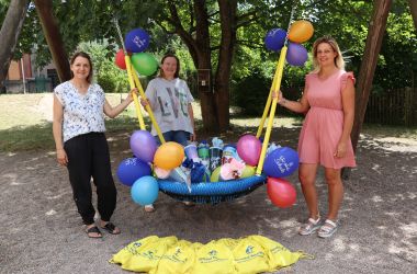 Drei Frauen stehen an einer Netzschaukel. Auf der Schaukel liegen Zuckertüten und Luftballons.