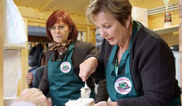 Zwei Frauen in grünen Schürzen heben Kuchen auf einen Teller.