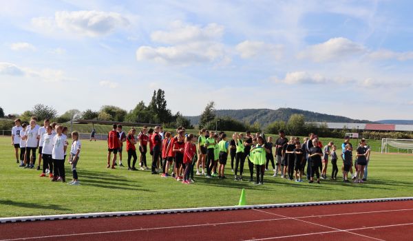 Kinder in unterschiedlichen Trikots stehen in Reihen nebeneinader auf einem Sportplatz.