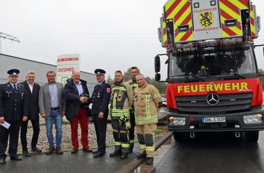 Feuerwehrmänner stehen vor einer Firma und nehmen eine Spende in Empfang.