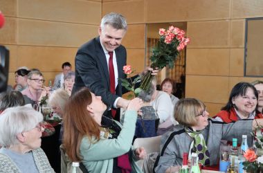 Frauen sitzen an gedeckten Tischen. Ein Mann verteilt Rosen. Es ist der Bürgermeister Dr. Heiko Voigt.