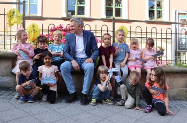 Vor einem Gartenzaun sitzen Kinder. In der Mitte sitzt der Bürgermeister Stadt Sonneberg Dr. Heiko Voigt.