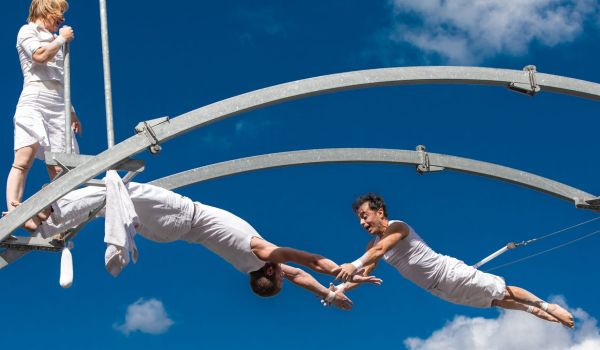 Drei Hochseilartisten turnen an einer brückenartigen Metallkonstruktion hoch in der Luft.