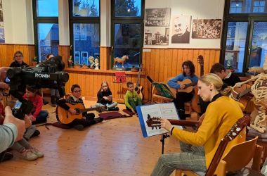 Kinder und Erwachsene sitzen im Kreis und musizieren.