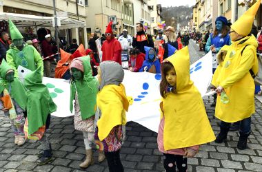 Kinder und Erwachsene sind als Mensch-ärgere-dich-nicht-Figuren gekleidet und tragen ein zugehöriges Spielbrett.