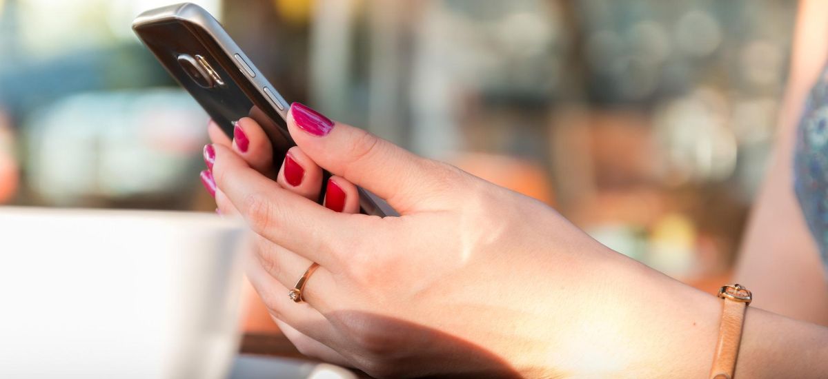 Weibliche Hände halten ein Smartphone in der Hand.