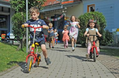 Kinder fahren auf Laufrädern einen Weg entlang.