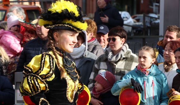Kostümierte Kinder und Erwachsene stehen an der Straße und beobachten den Umzug.