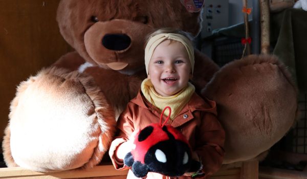 Ein Kind hält einen Marienkäfer aus Plüsch in den Händen und lacht. Im Hintergrund sitzt ein großer Teddybär.