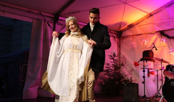 Eine Frau als Christkind gekleidet tanzt mit einem Mann auf einer Bühne.