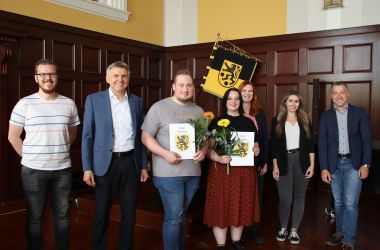 Sieben Personen stehen in einer Reihe nebeneinander. Davon halten Drei eine Mappe und eine Blume in den Händen. Es sind die neuen Auszubildenden der Stadt Sonneberg.