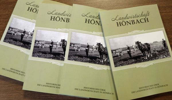 Vier Bücher mit der Aufschrift: Landwirtschaft Hönbach. Darunter ist ein altes Schwarz-Weiß-Foto, dass den Einsatz von Pferden in der Landwirtschaft zeigt.