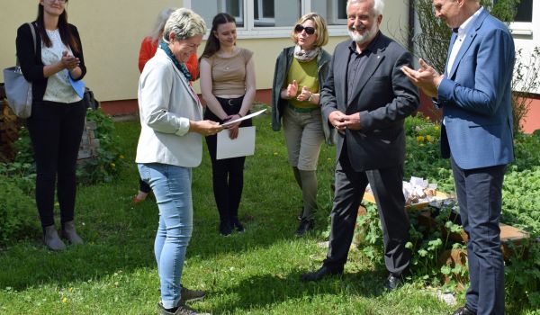 Zwei Männer überreichen eine Urkunde an eine Frau.