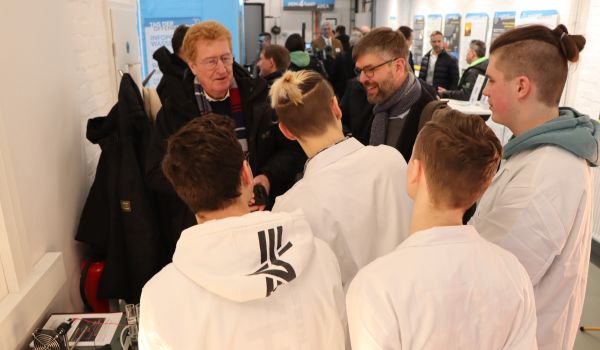 Jugendliche in weißen Kitteln erklären Experimente für Interessierte.