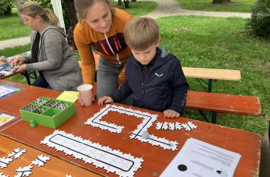 Ein Junge steht vor einem Puzzle mit einer schwarzen Linie. Darauf fährt ein Miniroboter.