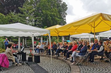 In einem Park sitzt Publikum und spielt eine Frau Klavier.