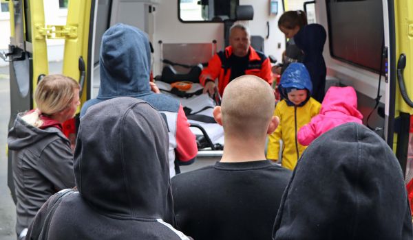 Kinder und Erwachsene stehen vor einem Rettungswagen mit geöffneter Kofferraumtür.