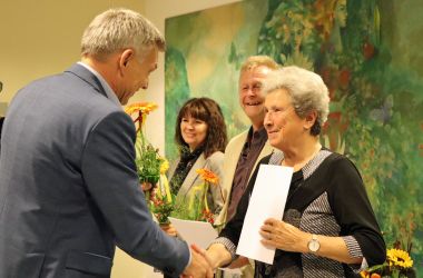 Der Bürgermeister Dr. Heiko Voigt überreicht eine Urkunde und Blumen an einen Mann und zwei Frauen.