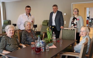 Drei Seniorinen sitzen an einem Tisch. Daneben stehen Mitarbeiter und der Bürgermeister der Stadt Sonneberg.