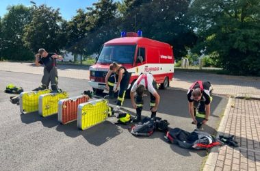 Mitglieder der Feuerwehr ziehen ihre Ausrüstung an. Dahinter steht ein Feuerwehrauto.