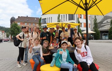 Eine Gruppe Kinder sitzt auf bunten Hockern unter einem gelben Schirm.