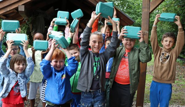 Kinder halten eine Brotdose in die Höhe.