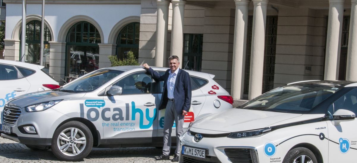 Wasserstoff-Autos stehen auf dem Platz vor dem Rathaus. In der Mitte steht der Bürgermeister der Stadt Sonneberg Dr. Heiko Voigt.