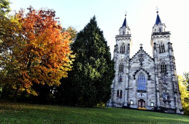 Eine Kirche mit zwei Türmen auf einem grünen Hügel mit Bäumen.