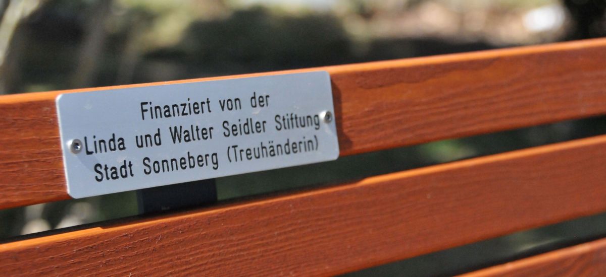 An einer Bank ist ein Metallschild angebracht. Es hat die Aufschrift: Finanziert von der Linda und Walter Seidler Stiftung Stadt Sonneberg (Treuhänderin).