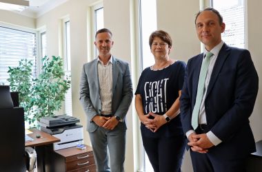 Zwei Männer und eine Frau stehen in einem Büro vor einer Fensterfront.