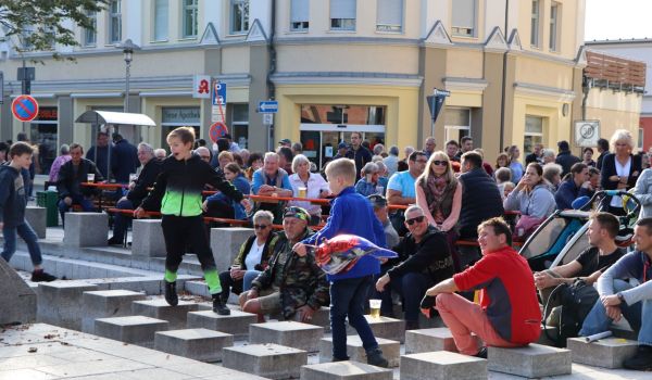 Viele Menschen sitzen draußen auf Bänken in der Innenstadt. Es scheint die Sonne.