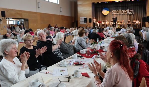 Frauen sitzen an gedeckten Kaffeetischen und klatschen in die Hände.