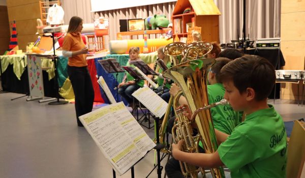 Eine Gruppe von Kindern mit Instrumenten sitz vor einer Bühne.
