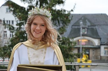 Eine Frau ist als Christkind gekleidet. Im Hintergrund ist der Bahnhof der Stadt Sonneberg.
