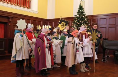 Kinder sind als Sternsinger gekleidet. Sie stehen in einem Saal und singen.