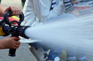 Zwei Hände halten einen Feuerwehrschlauch. Der Feuerwehrschlauch spritzt Wasser.