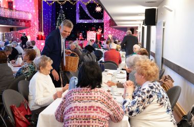 Frauen sitzen an gedeckten Kaffeetischen. Der Bürgermeister Dr. Heiko Voigt verteilt Geschenke.