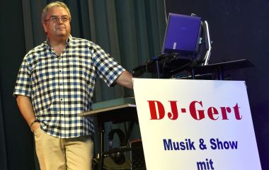 Ein Mann steht auf einer Bühne. Daneben steht ein Schild mit der Aufschrift: DJ-Gert Musik & Show