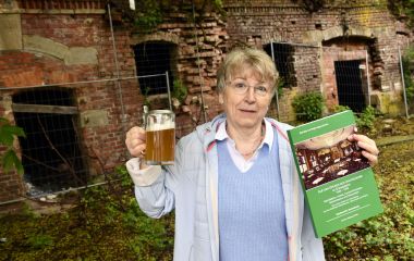 Eine Frau hält einen Krug mit Bier und ein grünes Buch in den Händen.