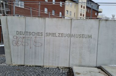 Auf einer Betonmauer steht Deutsches Spielzeugmuseum. Darunter 96515 mit Graffiti geschreiben.
