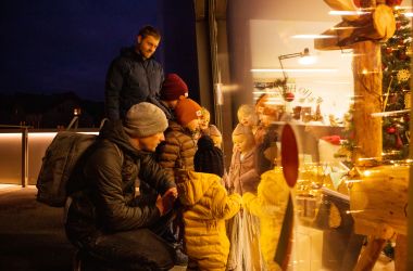 Eine Familie schaut am Spielzeugmuseum in eine weihnachtlich dekorierte Kulisse.